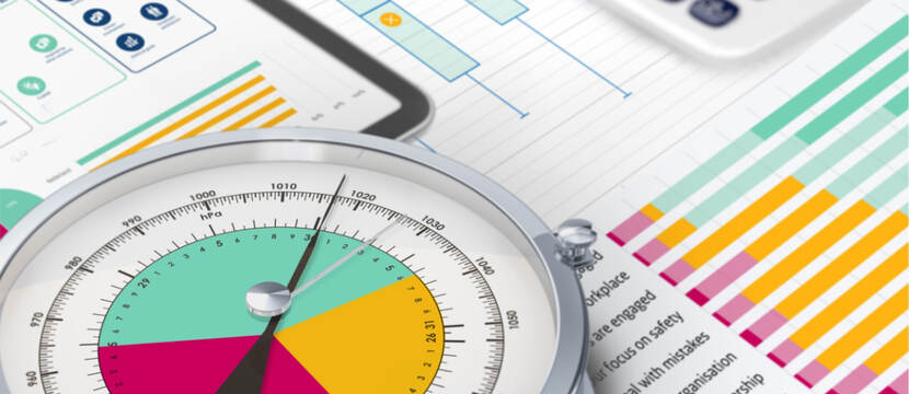 Een barometer die voor een tablet ligt en op een aantal papieren met daarop tabellen.